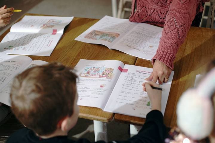A teacher guiding a workbook activity around a classroom table.