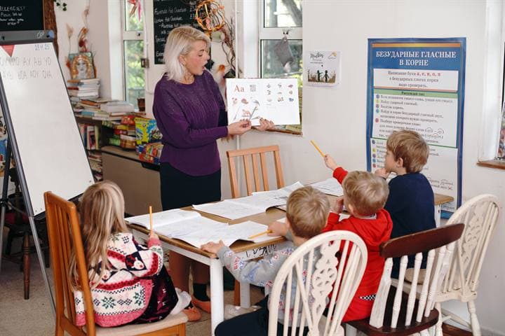 A teacher leading an alphabet lesson with children at a classroom table.