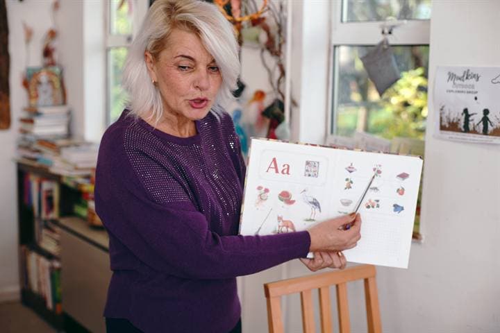 A teacher holding a Russian alphabet sheet during a classroom lesson.
