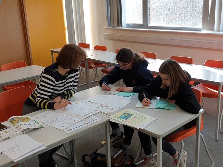 Children writing together at a classroom table.
