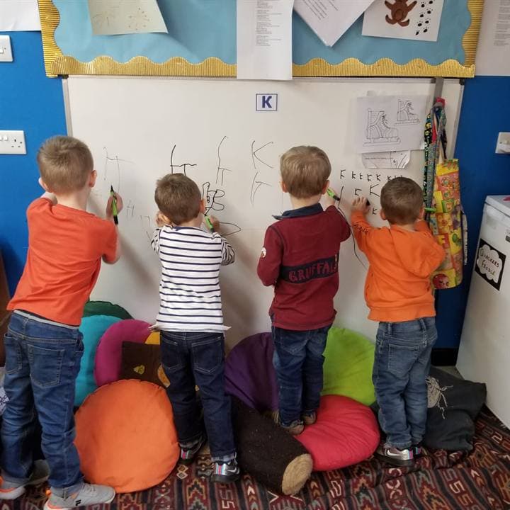 Children standing at a classroom whiteboard during a lesson.