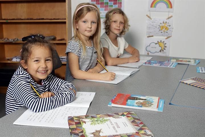 Children seated with Russian learning materials at a classroom table.