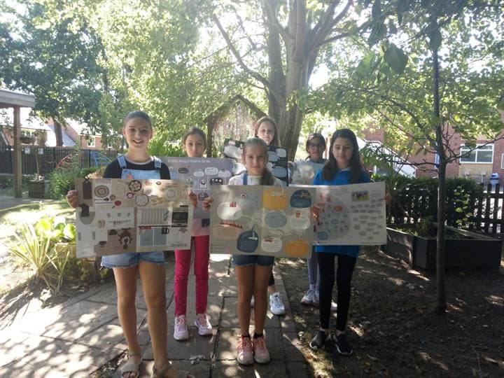 Children showing classroom artwork in an outdoor school setting.