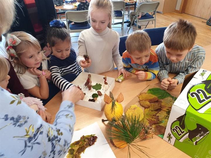 Children gathered around autumn craft materials on a classroom table.