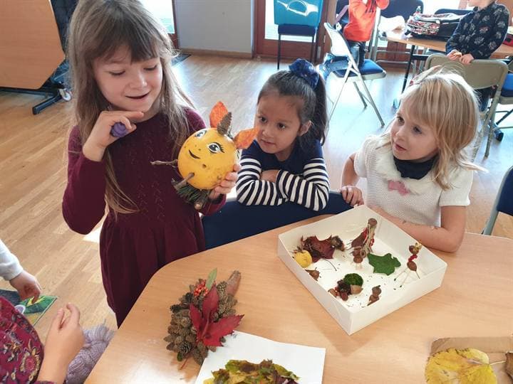 Children showing autumn craft work around a classroom table.
