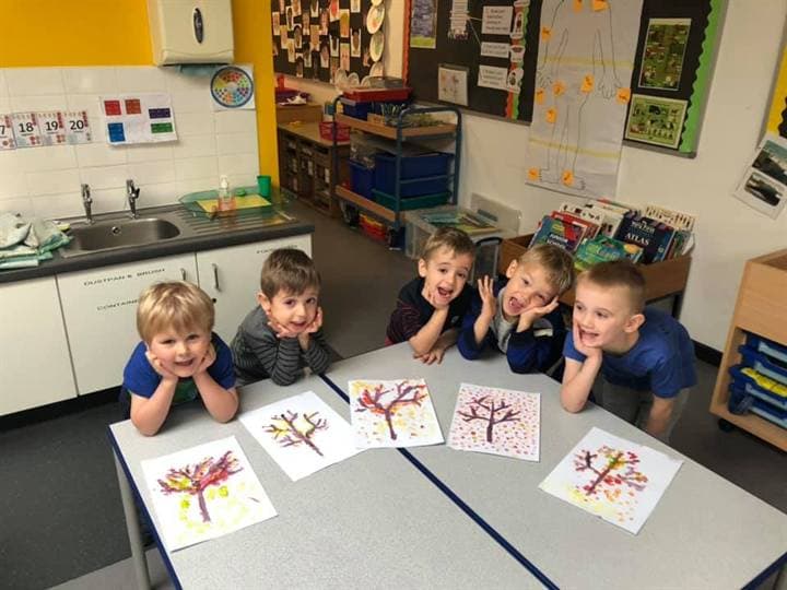 Children showing seasonal classroom artwork at a table.