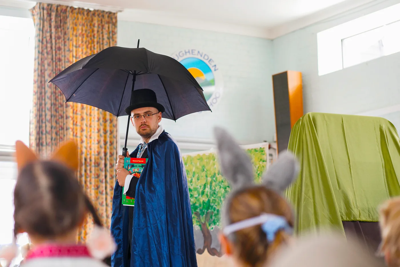 A costumed adult performer holding an umbrella during a school theatre event.